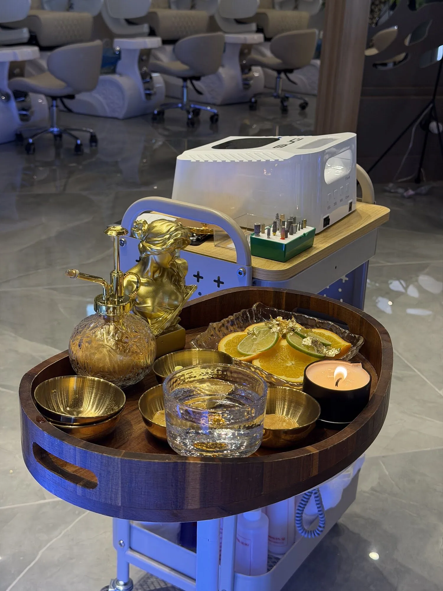 A pedicure tray at Zara Nail Bar Buckeye: gold bowls, orange and lime slices, a lit candle and a gold angel, ready beside the chairs.
