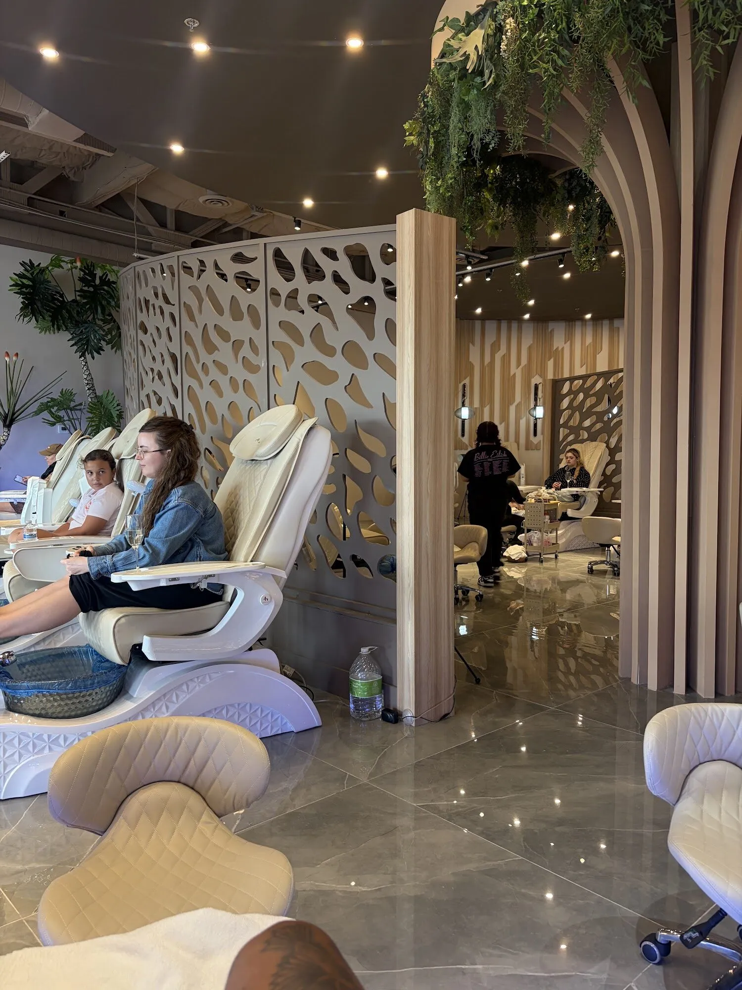Guests relaxing in cream pedicure chairs behind curved perforated screens at Zara Nail Bar Buckeye.