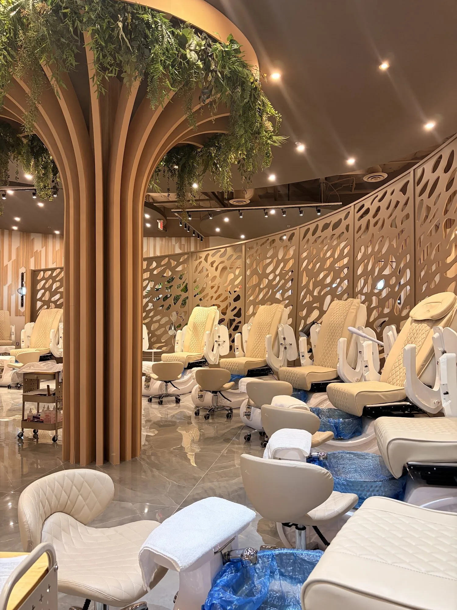 The pedicure lounge at Zara Nail Bar Buckeye, with cream chairs gathered around a sculpted wooden tree column and perforated screens.