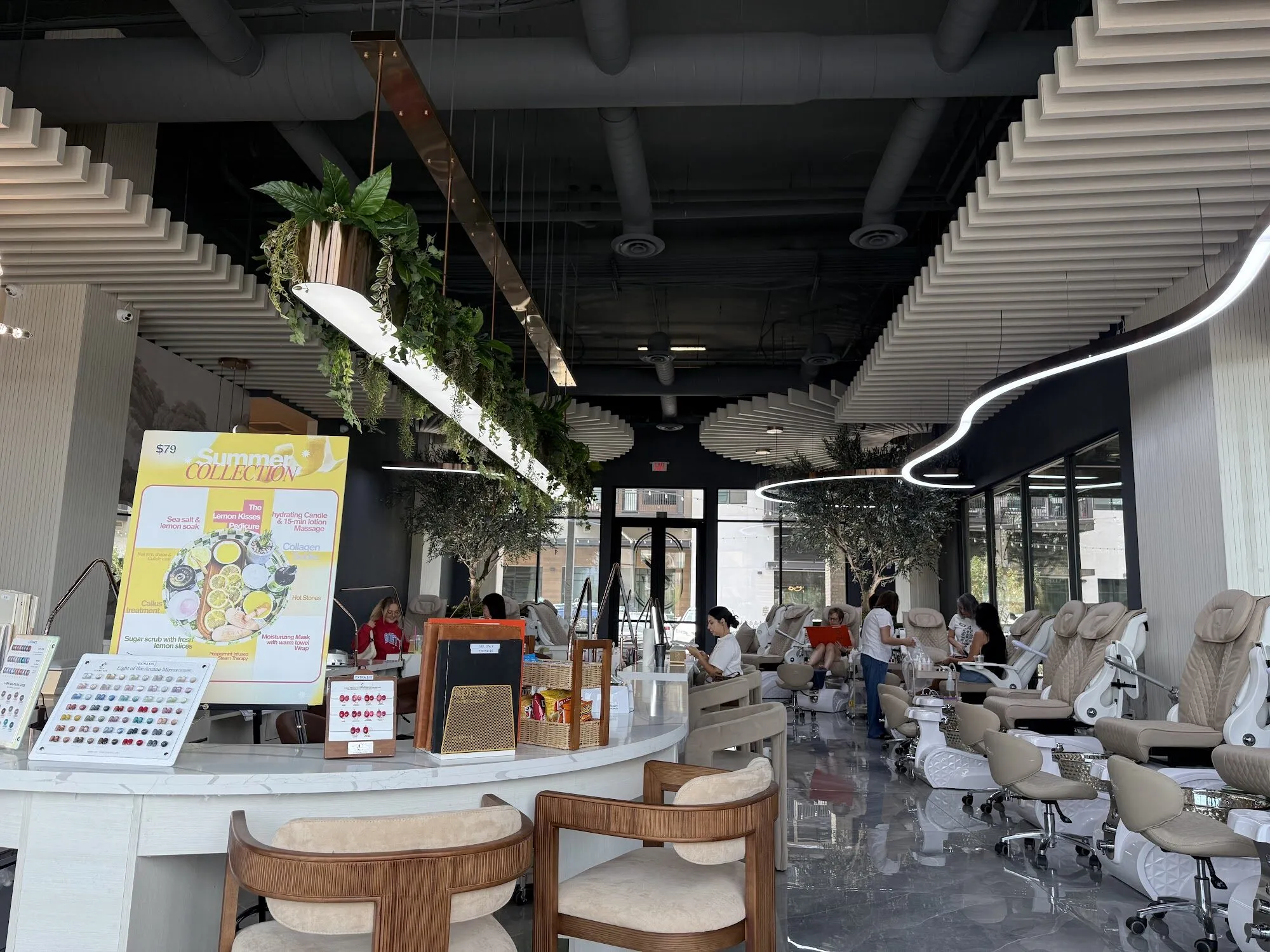 The curved manicure bar at Zara Nail Bar Higley with woven chairs, and the pedicure lounge under olive trees behind it.