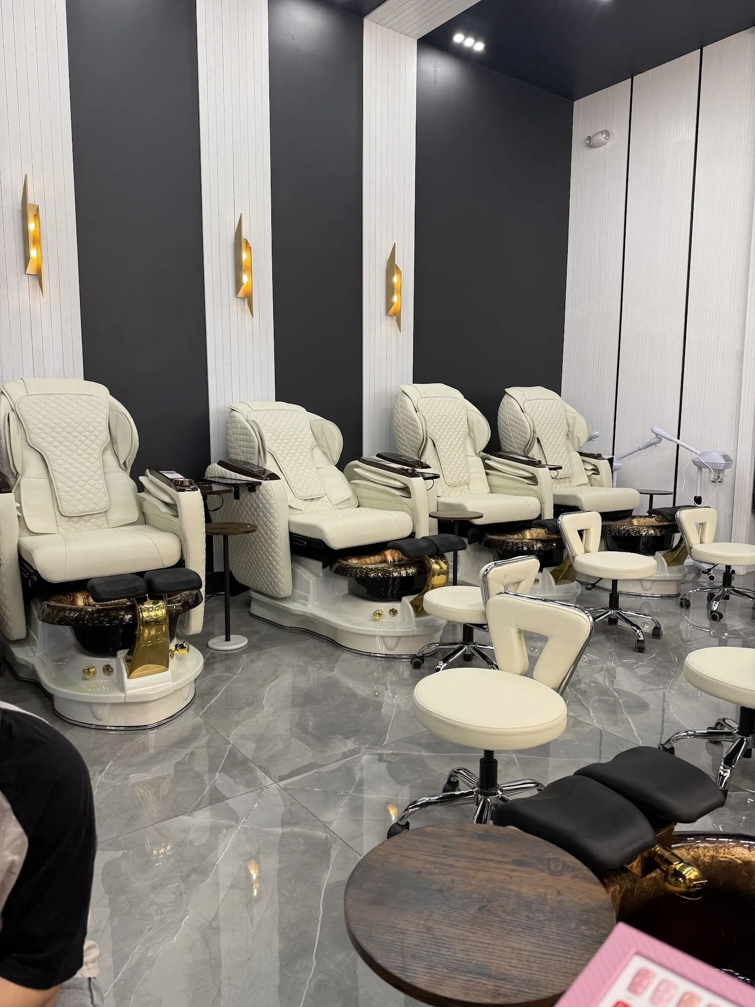 Cream pedicure chairs with gold bowls beneath brass wall lights at Zara Nail Bar Hudson.
