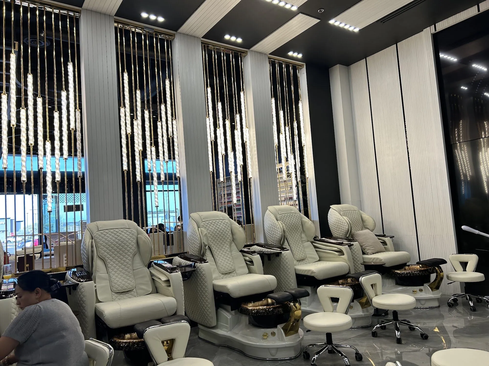 Cream pedicure chairs with gold bowls facing tall windows hung with strands of crystal at Zara Nail Bar Hudson.