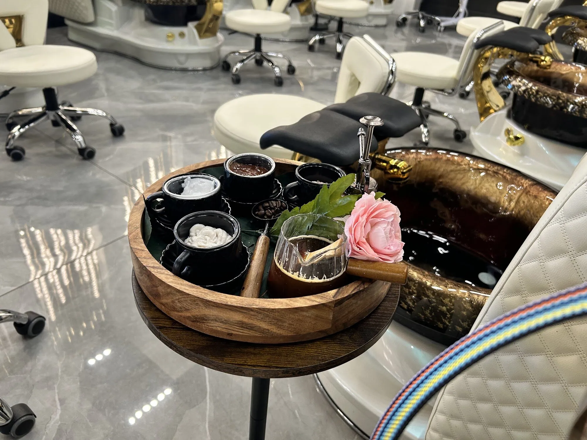 A pedicure tray at Zara Nail Bar Hudson: black bowls of scrub and mask, a glass of tea and a pink rose beside a gold pedicure bowl.
