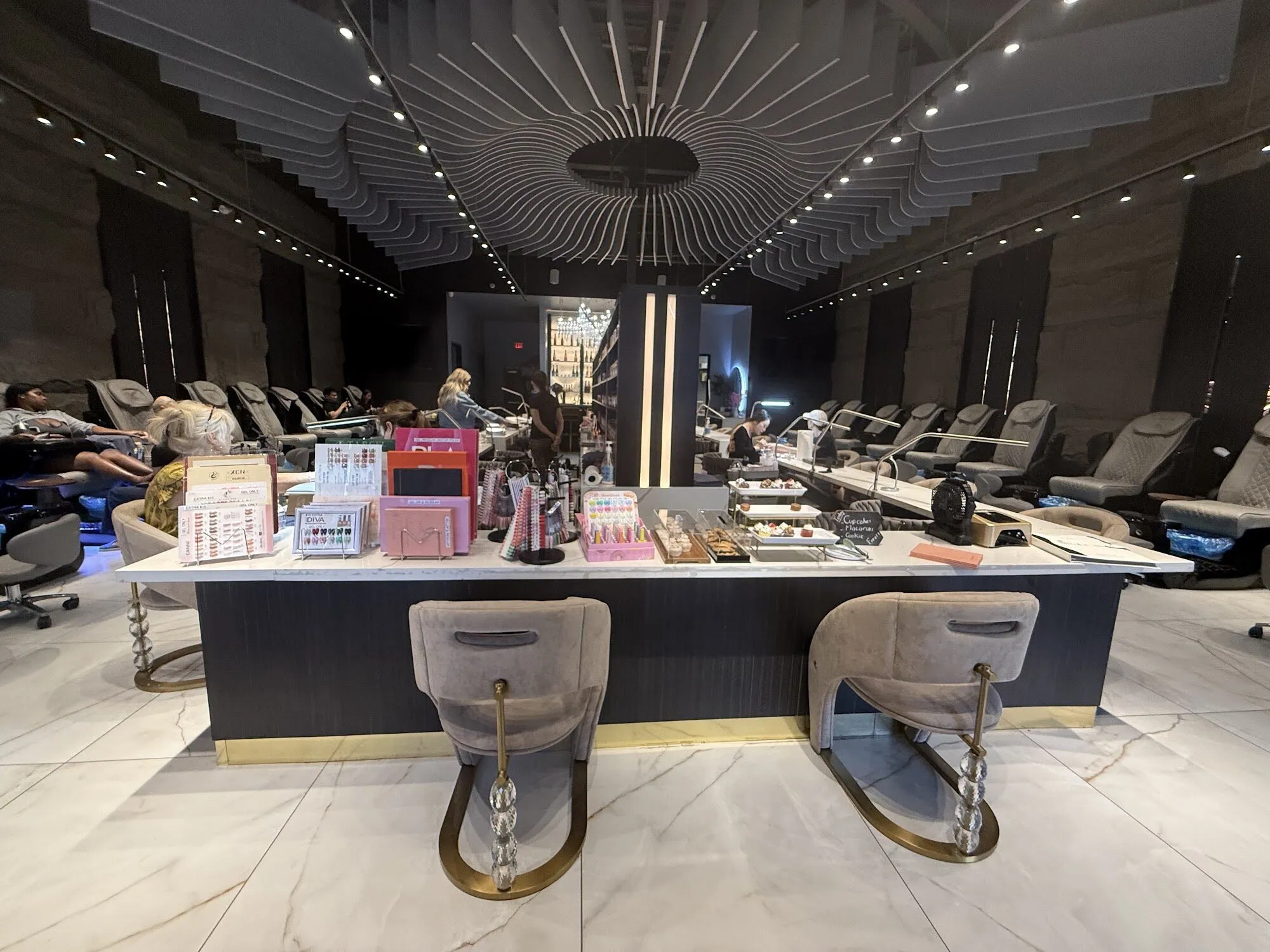 The manicure island at Zara Nail Bar Morrison, with sculpted grey chairs and pedicure chairs along both walls.