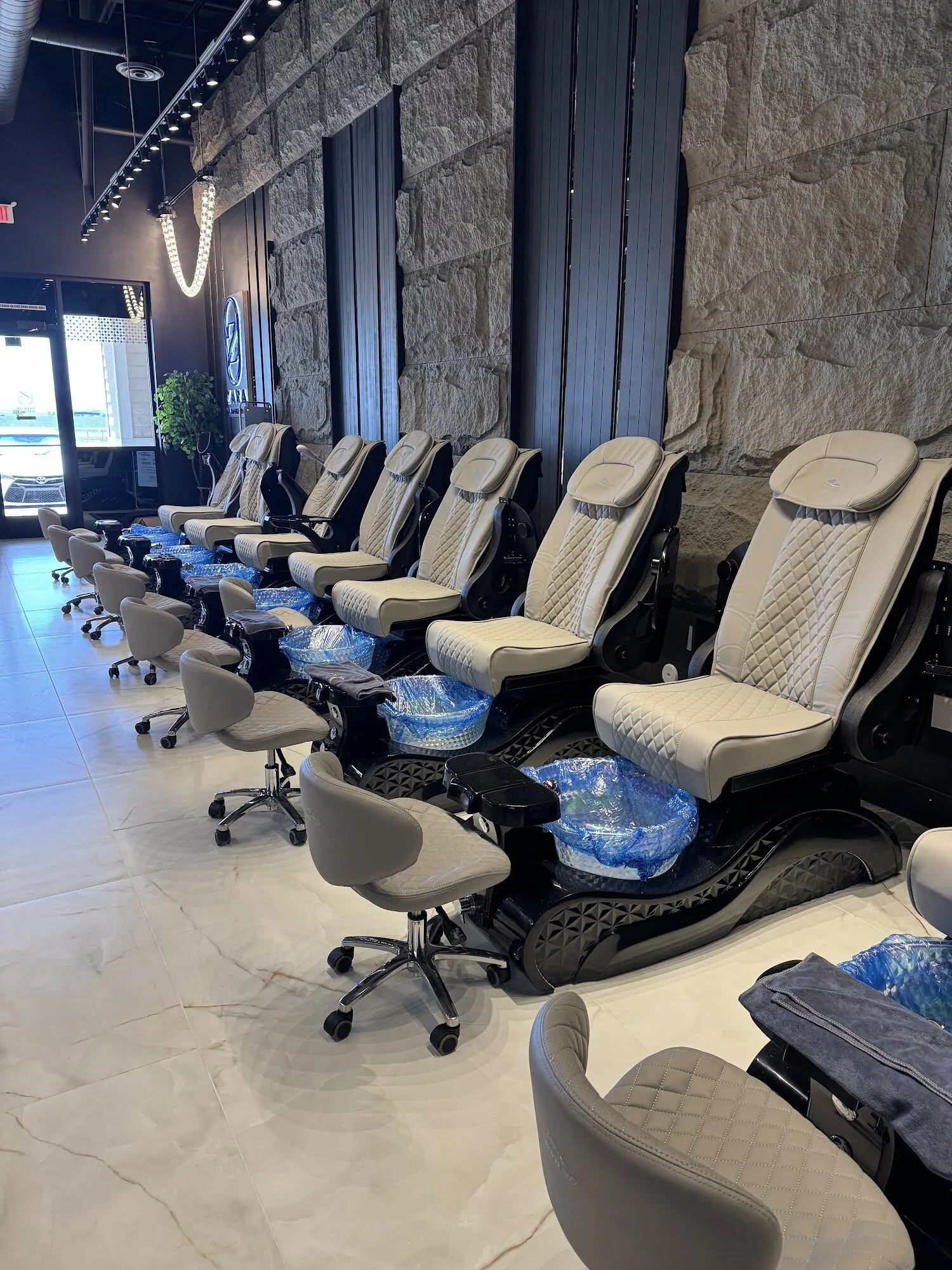 A row of quilted pedicure chairs along a stone wall at Zara Nail Bar Morrison, with string lights overhead.
