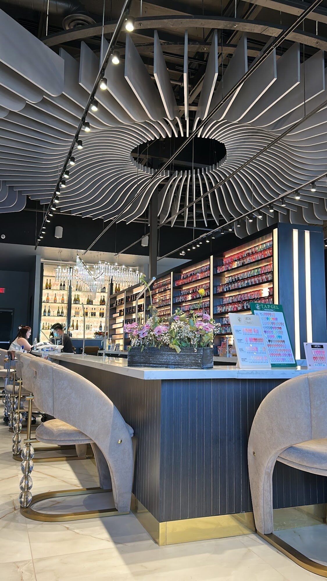 The manicure desk at Zara Nail Bar Morrison beneath a rippling slatted ceiling, with a wall of colour and the lit bar behind it.