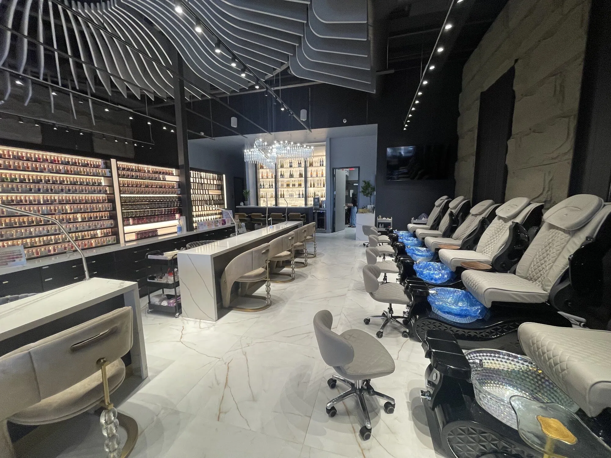 A wall of colour, the manicure tables and a row of quilted pedicure chairs along a stone wall at Zara Nail Bar Morrison.