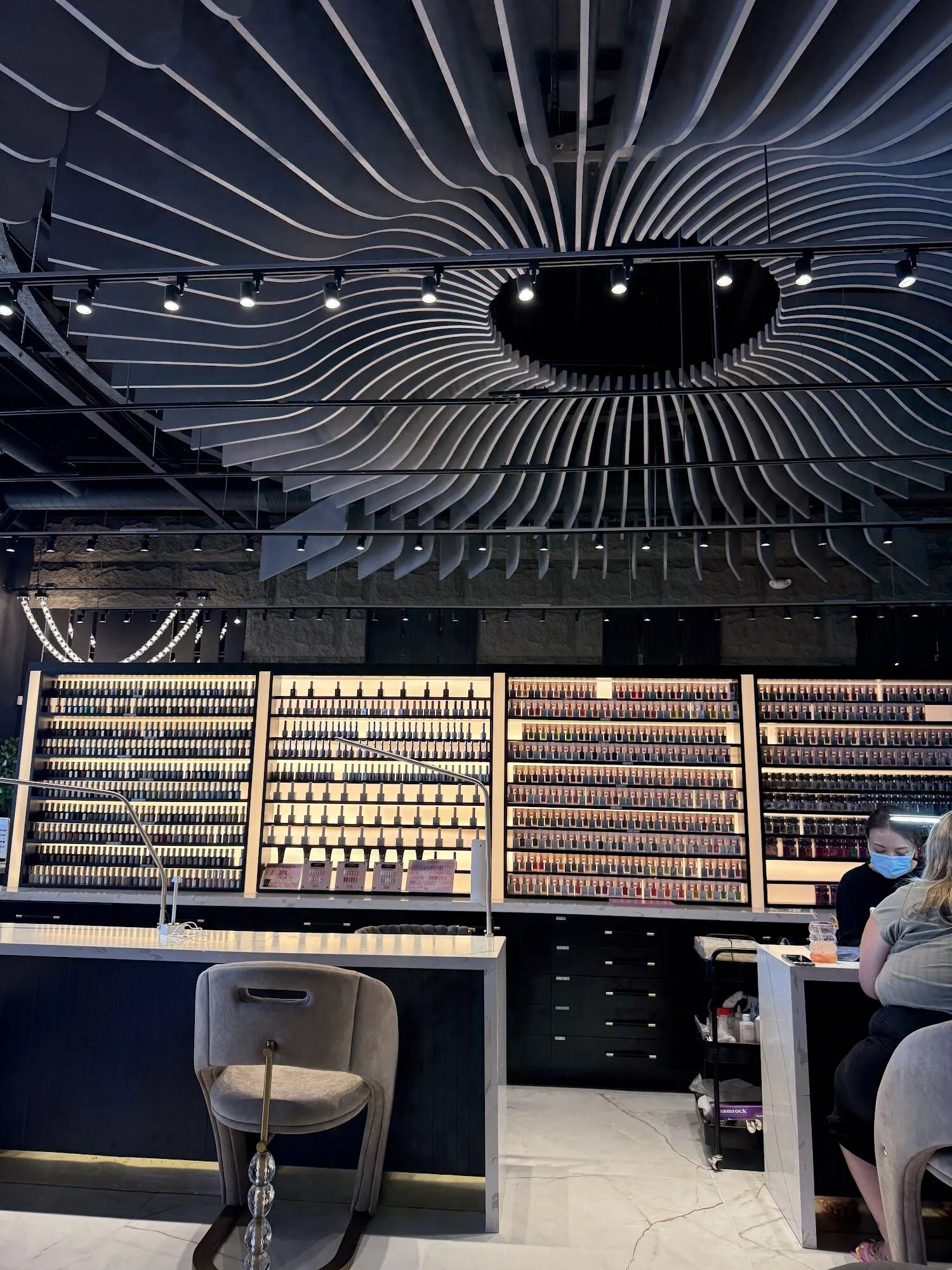 Rows of polish on a lit wall of colour beneath the rippling ceiling at Zara Nail Bar Morrison.