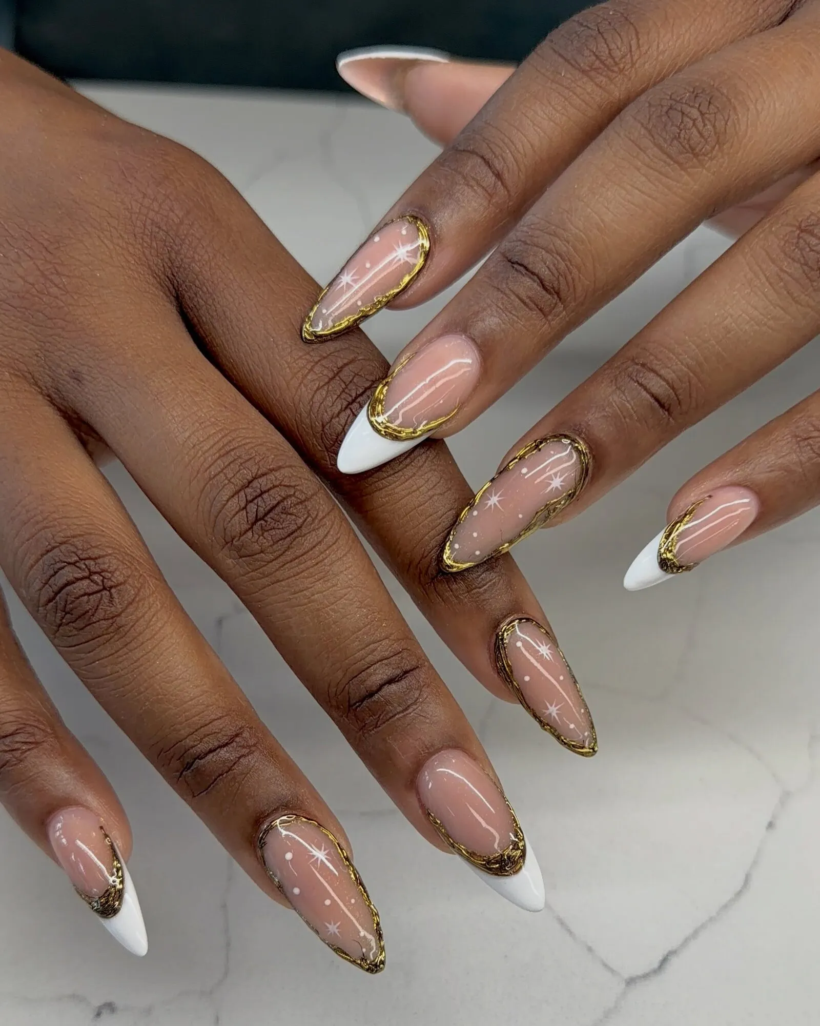 Long almond nails in a sheer nude with deep white French tips, gold chrome outlines and tiny white stars.