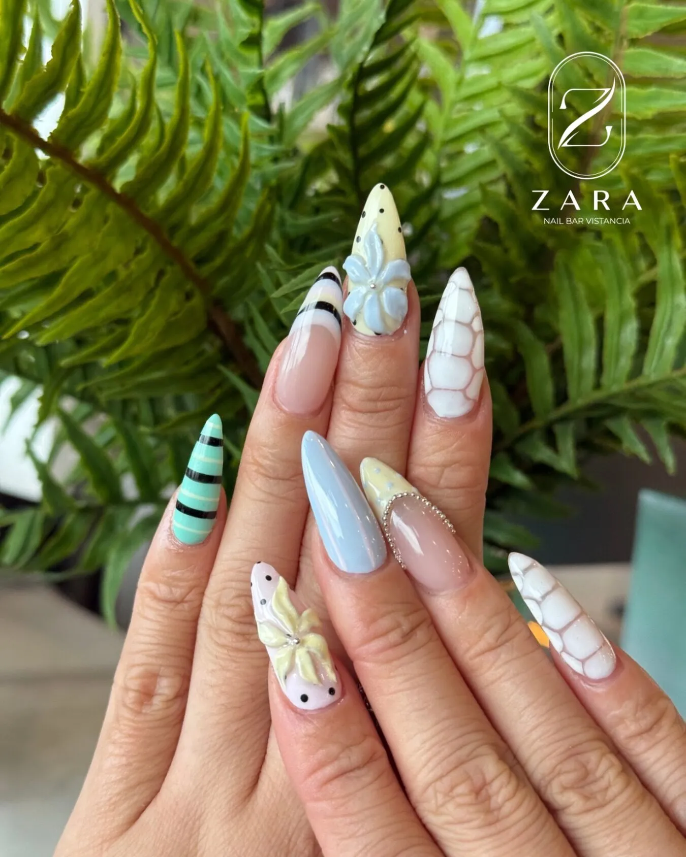 Stiletto nails in a pastel mix: mint stripes, sky blue, white marble and 3D butter-yellow flowers.