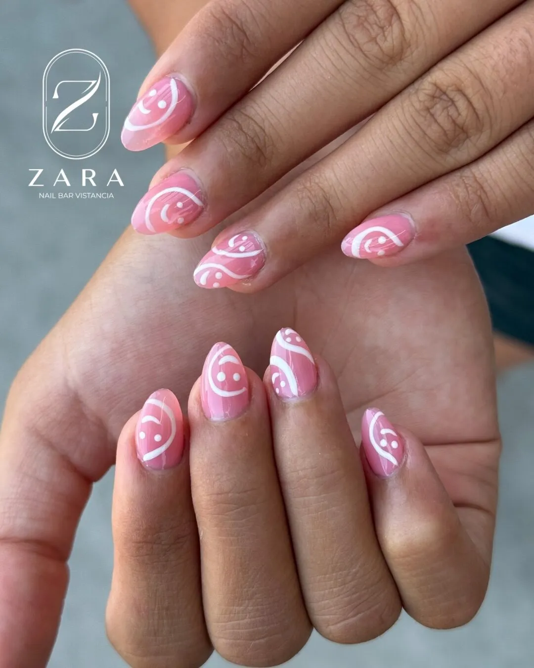 Short almond nails in bubblegum pink with hand-painted white smiley faces and swirls.