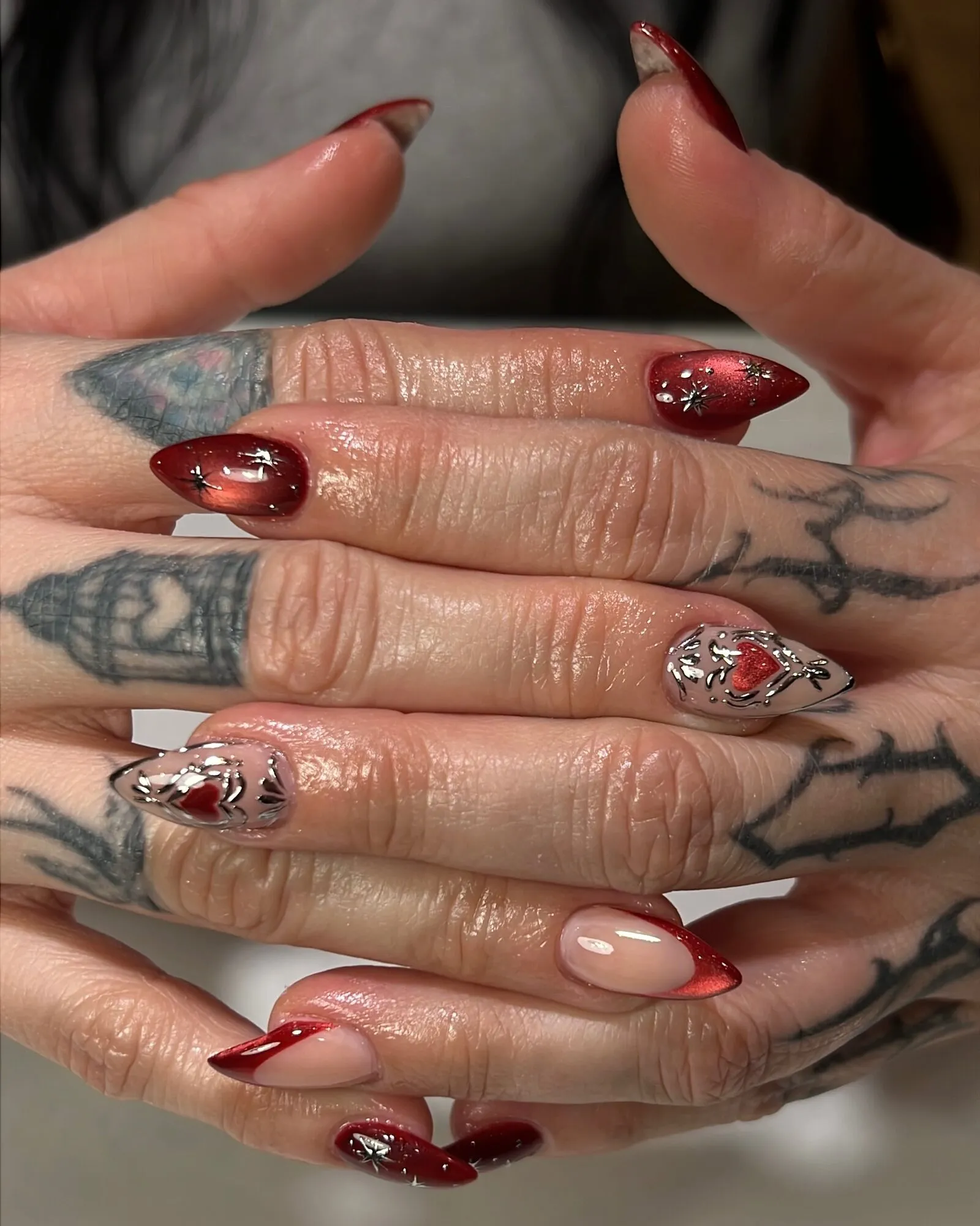 Almond nails with glossy red chrome French tips, red chrome accent nails and silver heart charms.