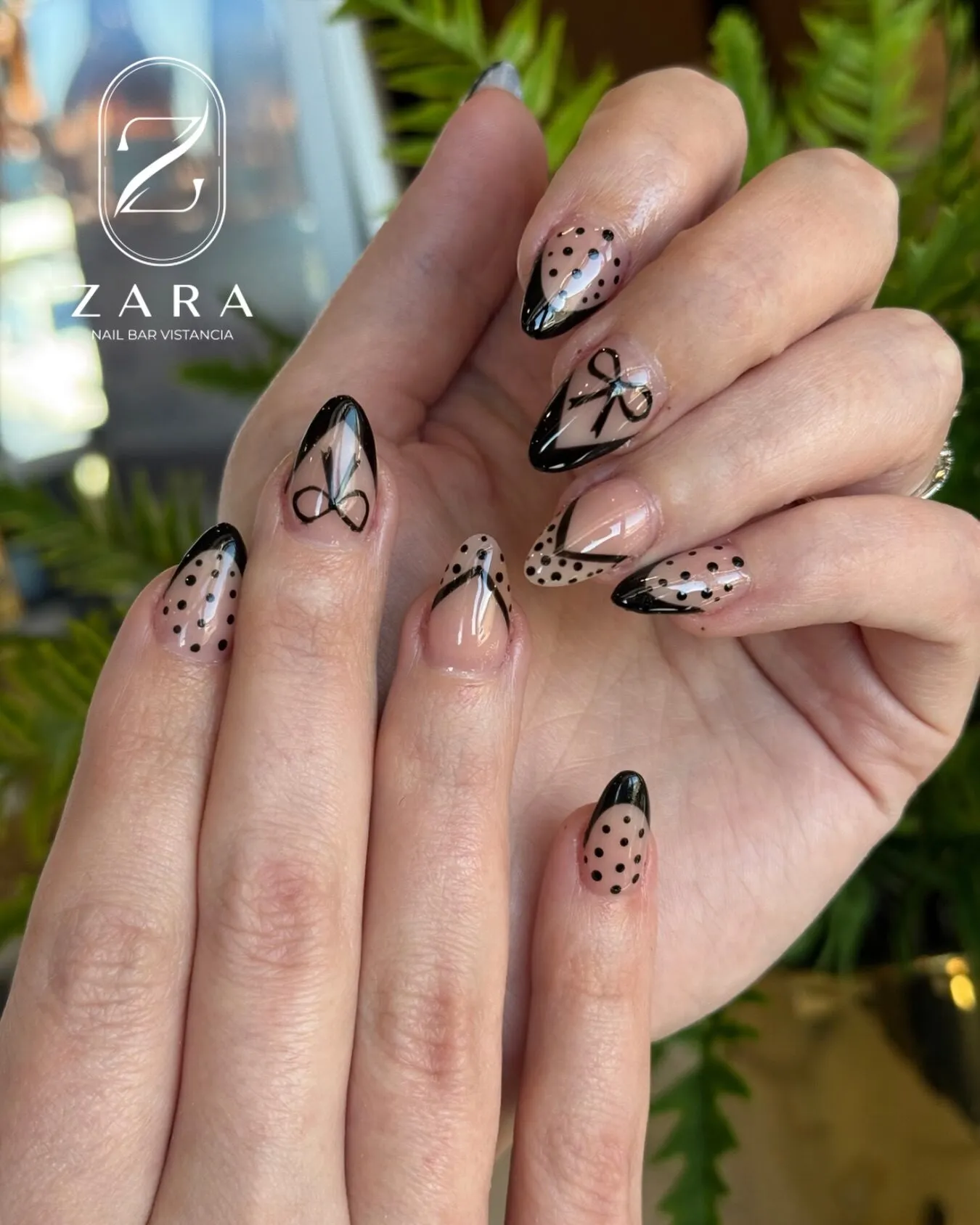 Sheer almond nails with hand-drawn black bows, polka dots and fine French tips.