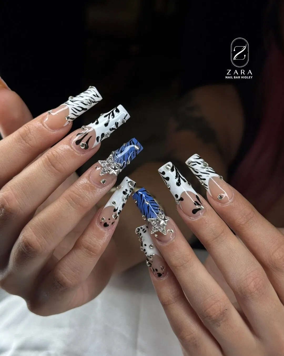 Long clear coffin nails with black and white zebra tips, a blue swirl accent, black florals and crystal star charms.