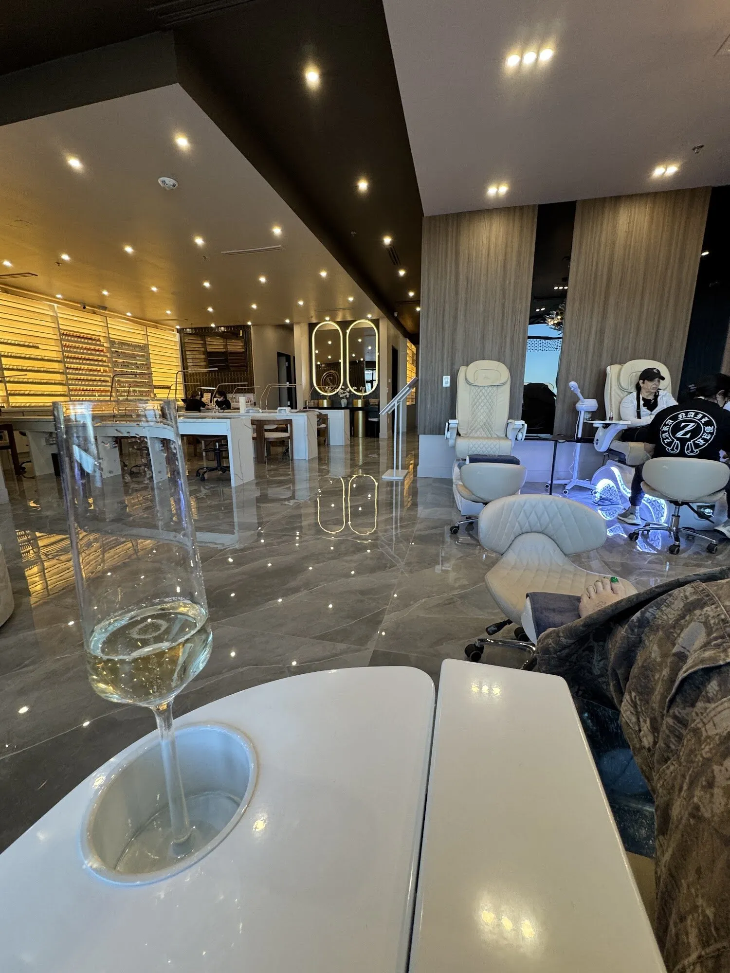 A glass of champagne in the cup holder of a manicure table at Zara Nail Bar Vistancia, looking across the pedicure lounge.