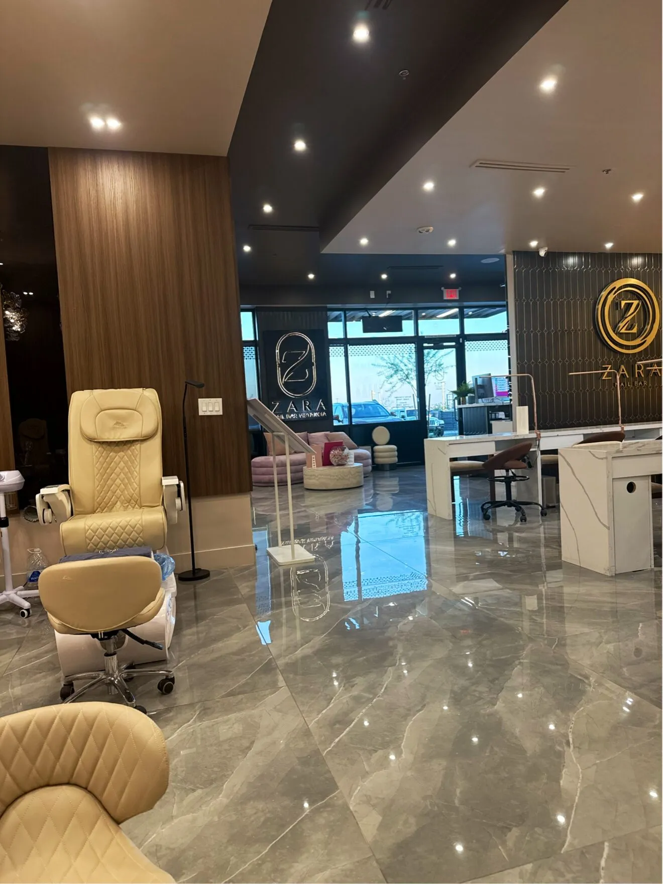 A quilted cream pedicure chair beside walnut panelling at Zara Nail Bar Vistancia, with the gold Zara sign across the room.