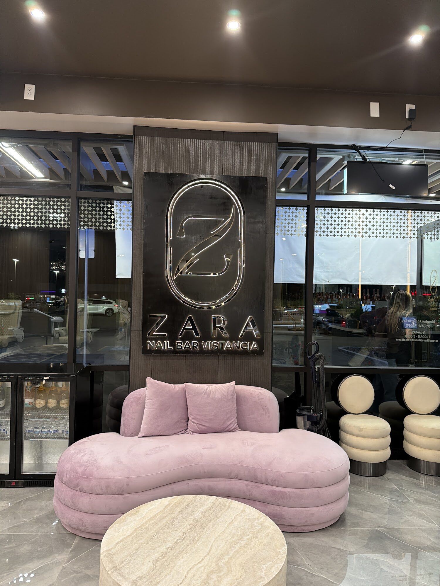 A blush velvet sofa and travertine table beneath the Zara Nail Bar Vistancia sign at the entrance.