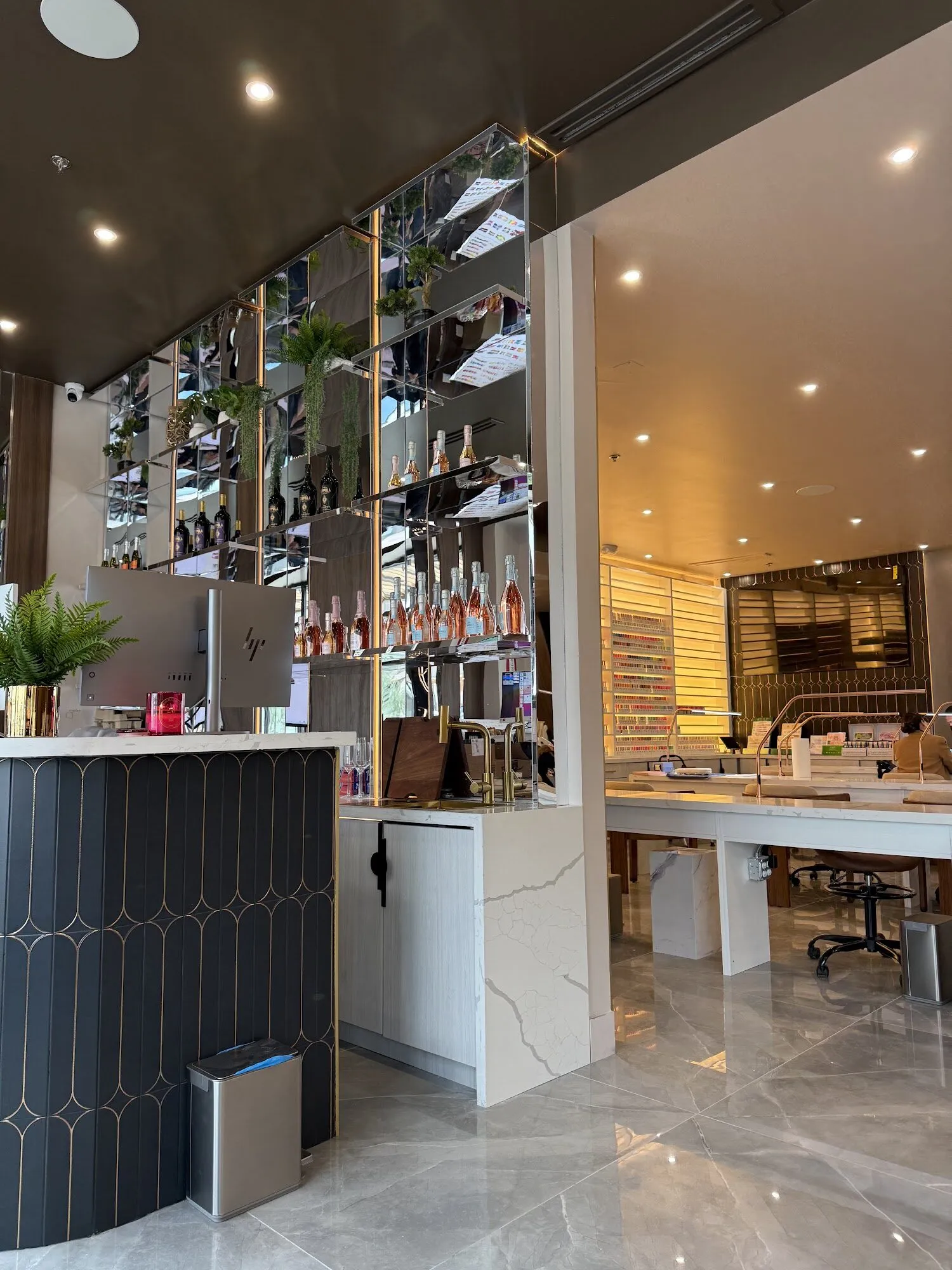 The front desk at Zara Nail Bar Vistancia: a navy panelled counter beneath glass shelves of bottles and plants.